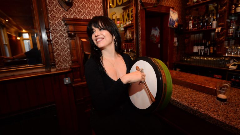 Imelda May playing a bodhrán in a pub setting, promoting her Raised on Songs & Stories: The Lock In tour