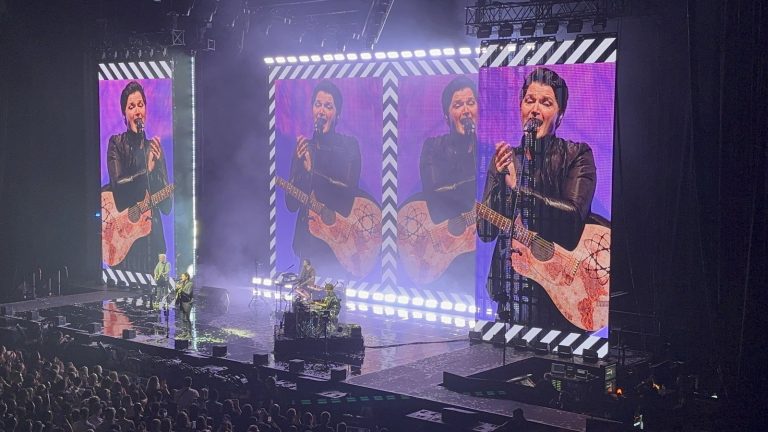 The Script performing on stage, with frontman Danny O'Donoghue on giant video screens above the band